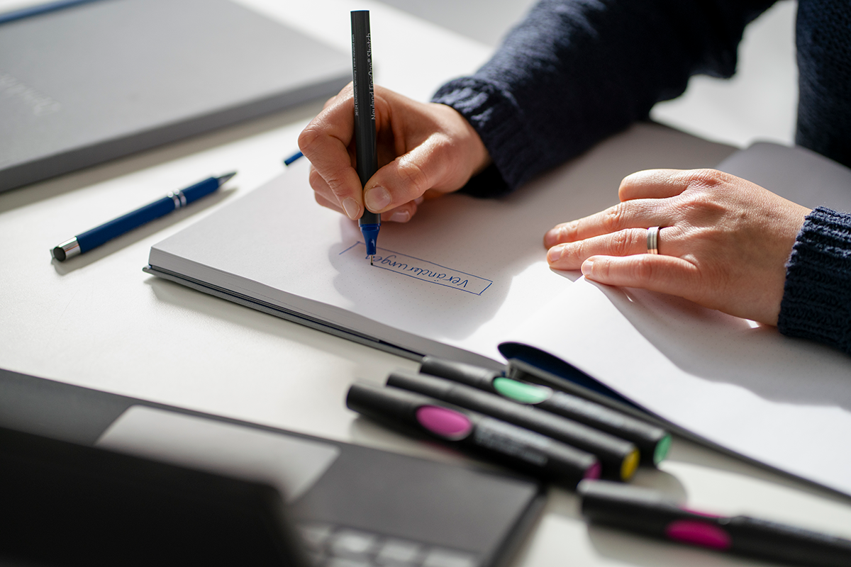 Konzentriertes Arbeiten im DenkArbeit Seminar – Hände beim Schreiben handschriftlicher Notizen mit farbigen Stiften