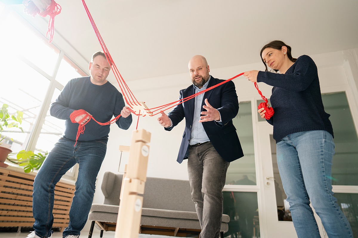 Dynamische Team-Übung mit roten Seilen bei DenkArbeit – drei Teilnehmende lösen gemeinsam eine koordinative Aufgabe aus der Froschperspektive